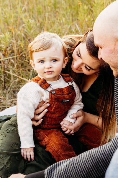 adorable baby boy in orange overalls being snuggled by parents. 