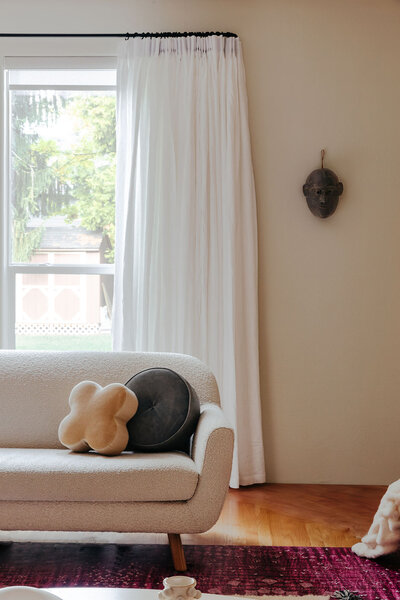  A love seat with cushions in front of window.