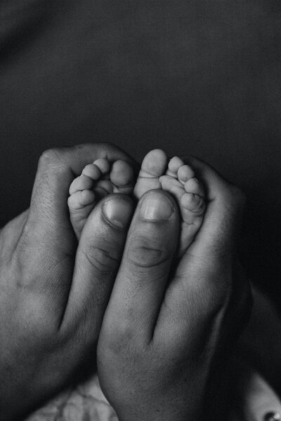 A black and white photo of a mans hands holding baby feet