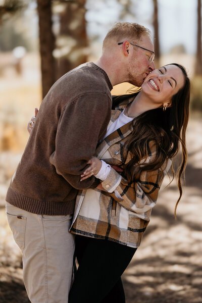 man kisses woman on cheek during Fall engagement photos.