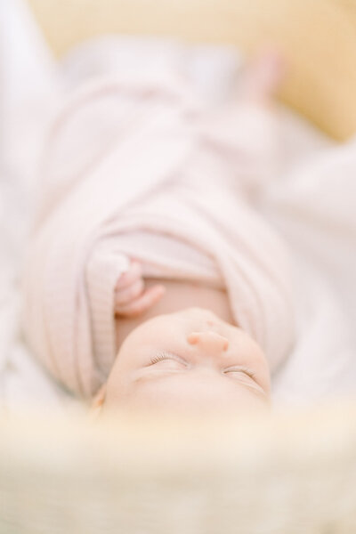 Baby in neutral pink wrap lying in a moses basket for a Tampa newborn photoshoot