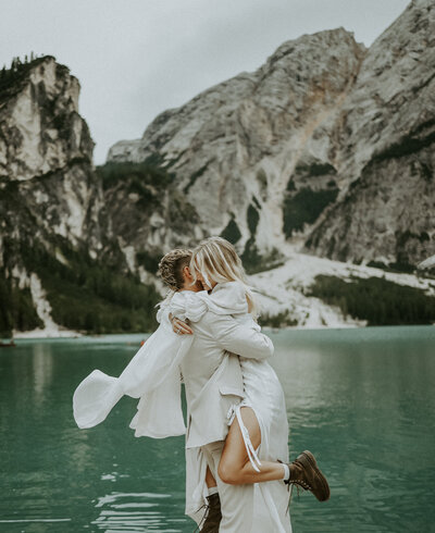 A bride and groom in wedding attire hug at Lago Di Braies in the Dolomites