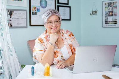 April sits at her desk with her crystals arranged in front of her, smiling at the camera