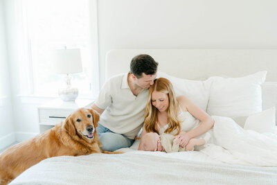 Mom and dad hold newborn baby and golden retriever on bed 