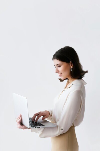 woman in white top standing and holding a laptop
