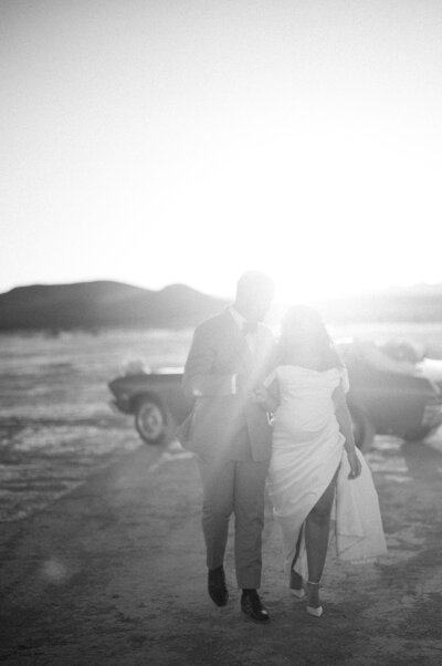 Bride smiles while the groom kisses her cheek in front of a white floral arch.