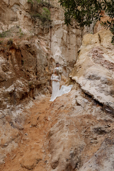 Adventure wedding couple walking hand-in-hand through a red rock canyon at golden hour.