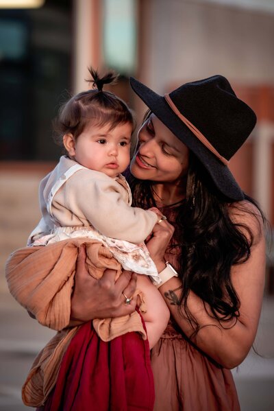 Mother in a black hat loving on her young daughter taken at a roof top carpark