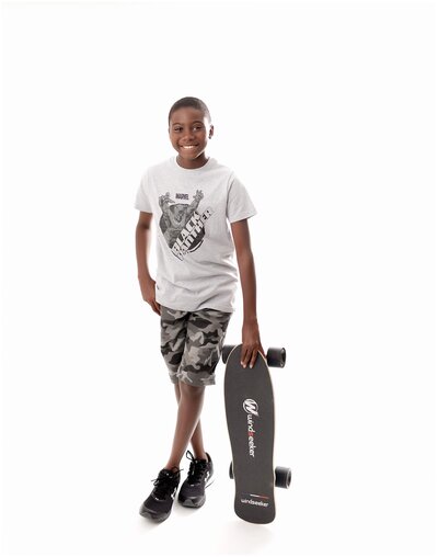 A boy posing for a portrait, showcasing his skateboard.
