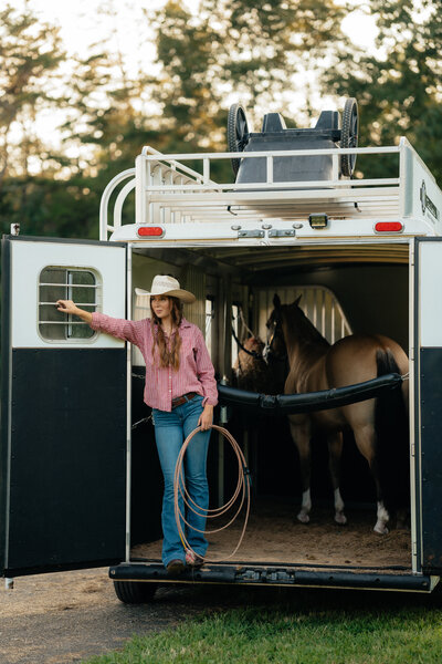woman standing outside a horse trailer looking off in the distance holding a rope
