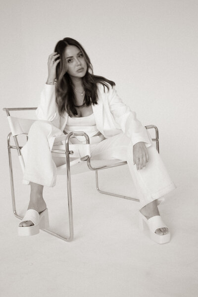 a professional 6 figure business woman dressed in a white business suit sitting in a chair and posing