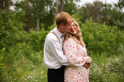 Engaged couple with his arms around hers in field