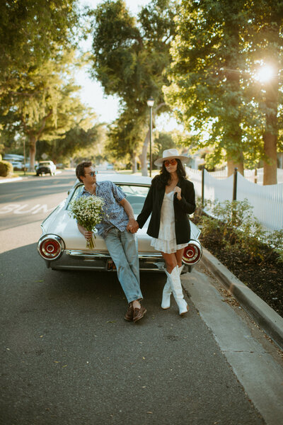 man and woman holding hands while leaning against classic car