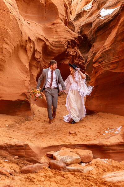 An eloping couple runs playfully through a red rock slot canyon near Antelope Canyon in Page, Arizona.