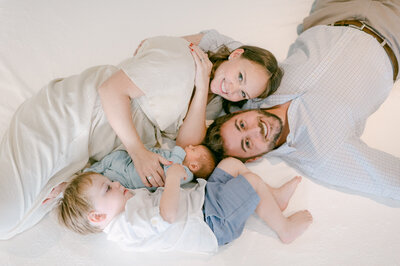 Whole Family laying down on the bed during their lifestyle newborn photo shoot