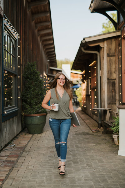 Shawna, owner of Hive and Harmony, walking with a cup of coffee and a laptop in her hands