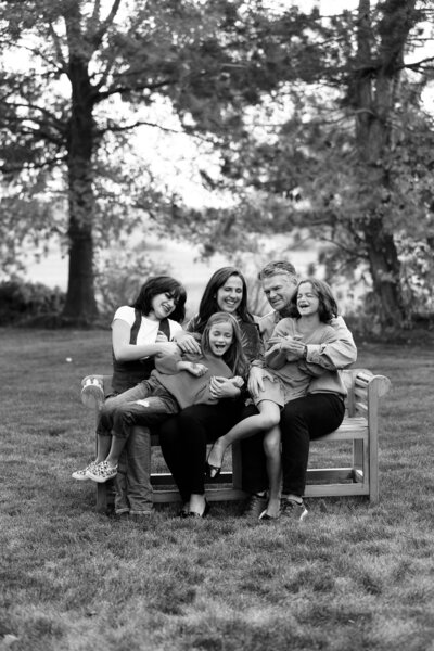 Family of 5 sitting on a bench in their yard laughing and tickling during photos with Boise Photographer Tiffany Hix