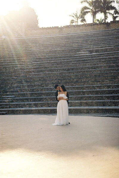 Bride and groom embracing in the amphitheater of Altos de Chavón, bathed in golden sunlight — cinematic destination wedding moment captured by Asia Pimentel Photography.