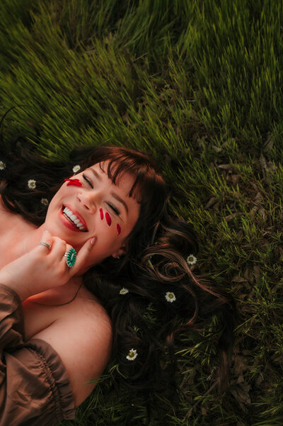 Motherhood solo moment of mom laying field with flowers in hair, smiling and laughing