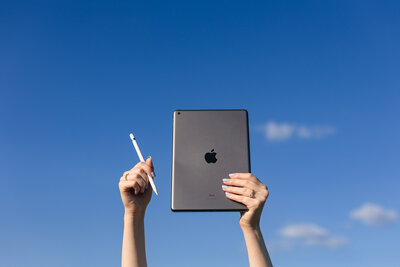 a woman holds her ipad and apple pencil in front of a clear blue sky