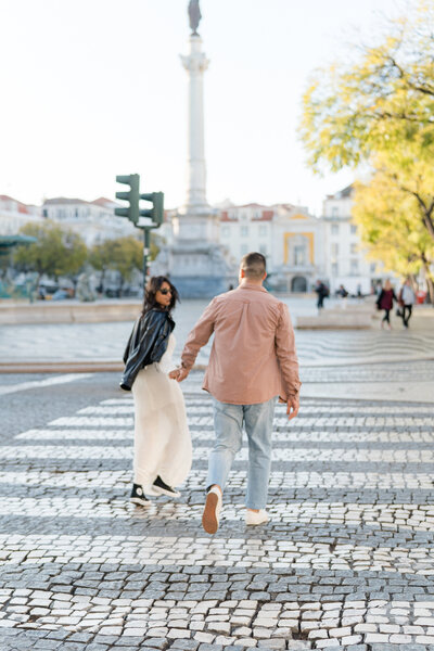 Engagement photos in Libson Portugal. Couple running across the street at sunrise.