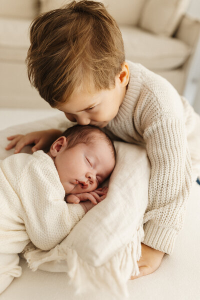 A little boy kissing his baby sisters hair taken during a newborn photoshoot in christchurch