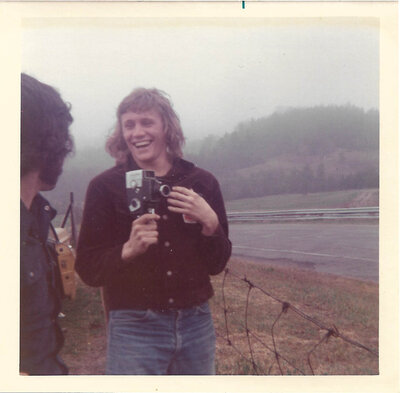 a man with a super 8 camera in his hand, laughing. 