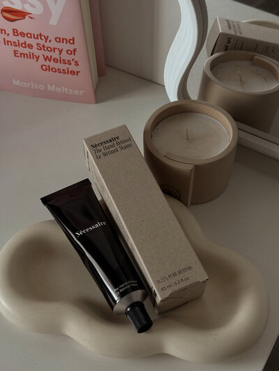 A curated flat-lay of beauty essentials, featuring a beige cloud-shaped jewelry holder, a minimalist skincare tube, and a small beige box. A candle, mirror, and book add to the warm, neutral-toned aesthetic. Created for Glow Beauty Studio’s social media strategy, this image reflects a refined and elegant brand identity.