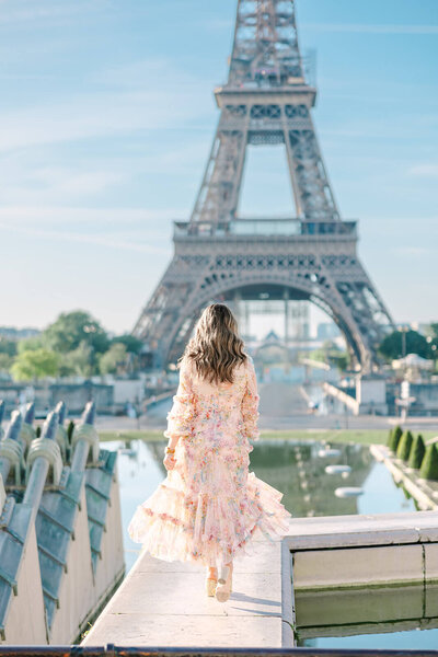 Mother in a floral dress facing away from the camera during a mother-daughter family photoshoot at the Eiffel Tower, captured at Trocadéro in Paris.