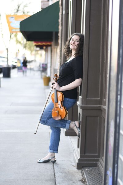 Seattle violin teacher Dr. Erika Burns leans against a wall with her violin.