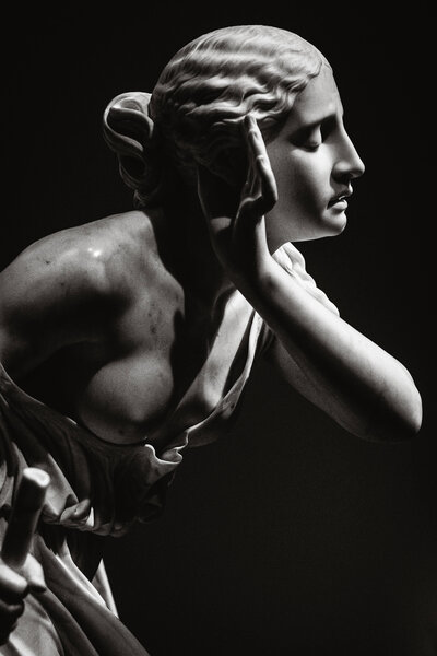 Black and white photo of classical marble statue of woman with hand up to ear