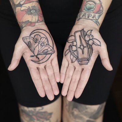 Handflata tatueringar av en fjäril, måne och flaska med bär.
