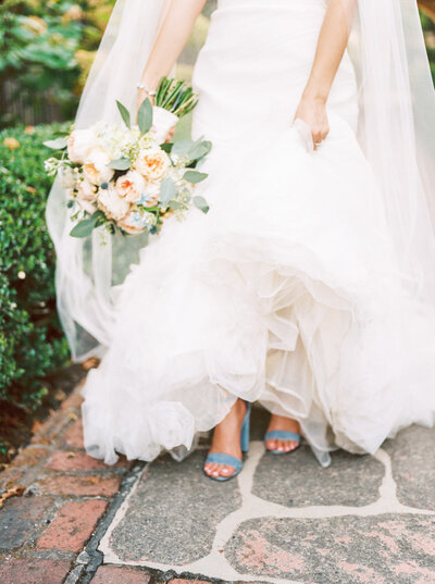 Bride holding pastel wedding bouquet with peach roses and blue accents