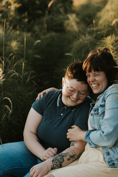 A couple sitting closely together, laughing in a grassy area taken in Seattle.