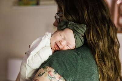 A newborn in a green hat resting contently against an adult's shoulder, captured perfectly by a skilled Pittsburgh photographer specializing in lifestyle photography.