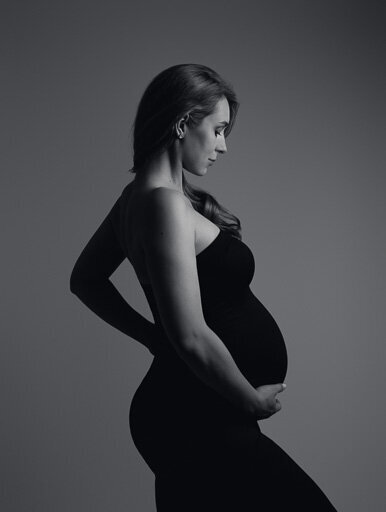 Pregnant woman in a black dress full height profile portrait.