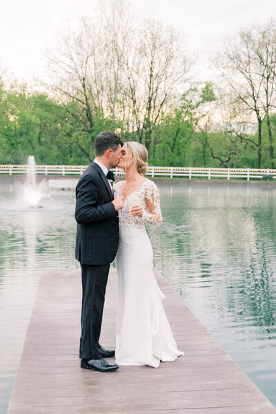 Bluestone Estate couple sharing a kiss with champagne in hand, celebrating their wedding day on a scenic dock.