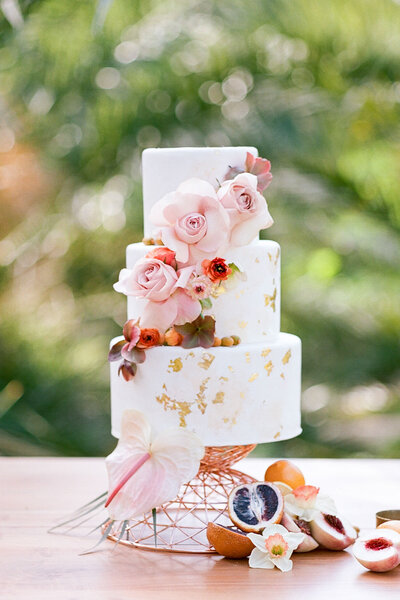 White and gold foil wedding cake with flowers and fruit decorating it