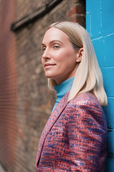 WOMAN IN PINK JACKET LEANING AGAINST WALL JO WOOD