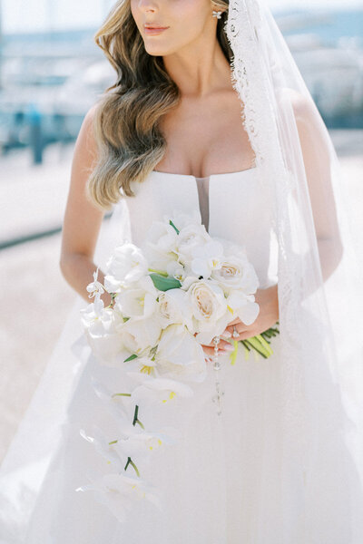 Close-up of bride’s cascading orchid bouquet and modern wedding gown with lace veil, captured in natural light