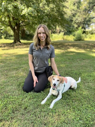 Dog trainer Michelle Pennarola sitting with a brown and white dog  in a park