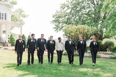 A group of groomsmen at John Joseph Inn walk on the front lawn. 