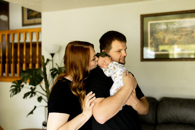 Father holding newborn baby while mother kisses baby's forhead