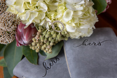 Close-up of wedding rings resting on a bouquet of white hydrangeas and protea, placed on custom vow books during a Yosemite elopement. Captured by Yosemite elopement photographers, this detail shot highlights the personal touches of an intimate wedding.