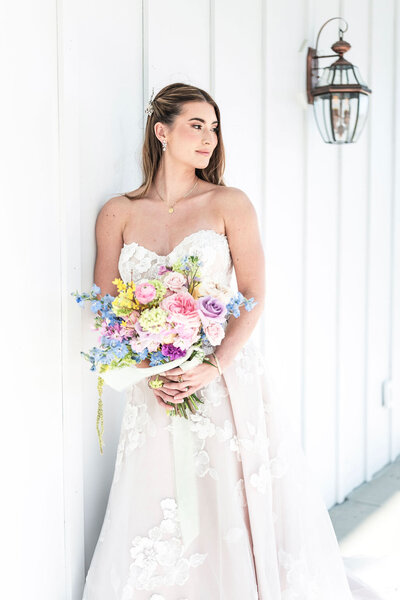 Bride in white dress and floral bouquet standing next to white wedding venue