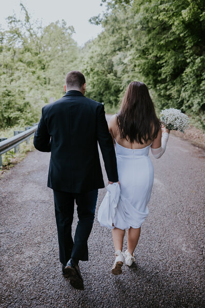 Bride and groom walk hand in hand down a quiet wooded road, captured by a Nashville elopement photographer after their intimate ceremony.