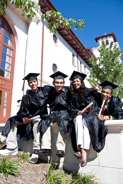 Group of college graduates smiling while wearing their cap and gown, celebrating their graduation.