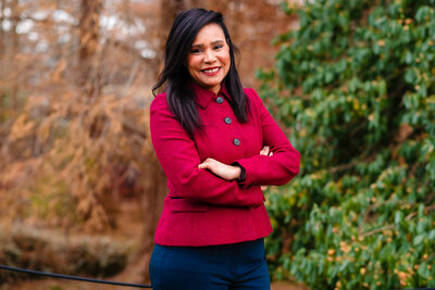 A woman in a black suit and purple blouse poses for a photo in front of a wood panel.