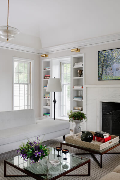 Boston interior decorators designed a modern living room in a historic Hingham home with a sleek sofa, mid-century table, and crisp white walls for a clean, timeless look.