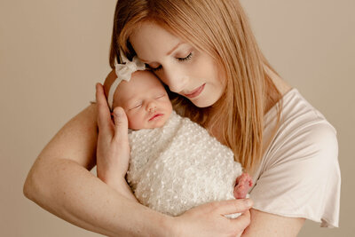 Newborn baby girl with hands on face laying on a pink background